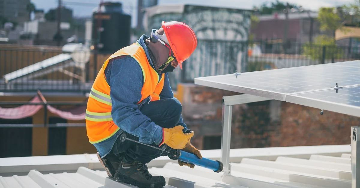 Technicien en équipement de sécurité installant des panneaux solaires sur un toit, garantissant l'efficacité énergétique.