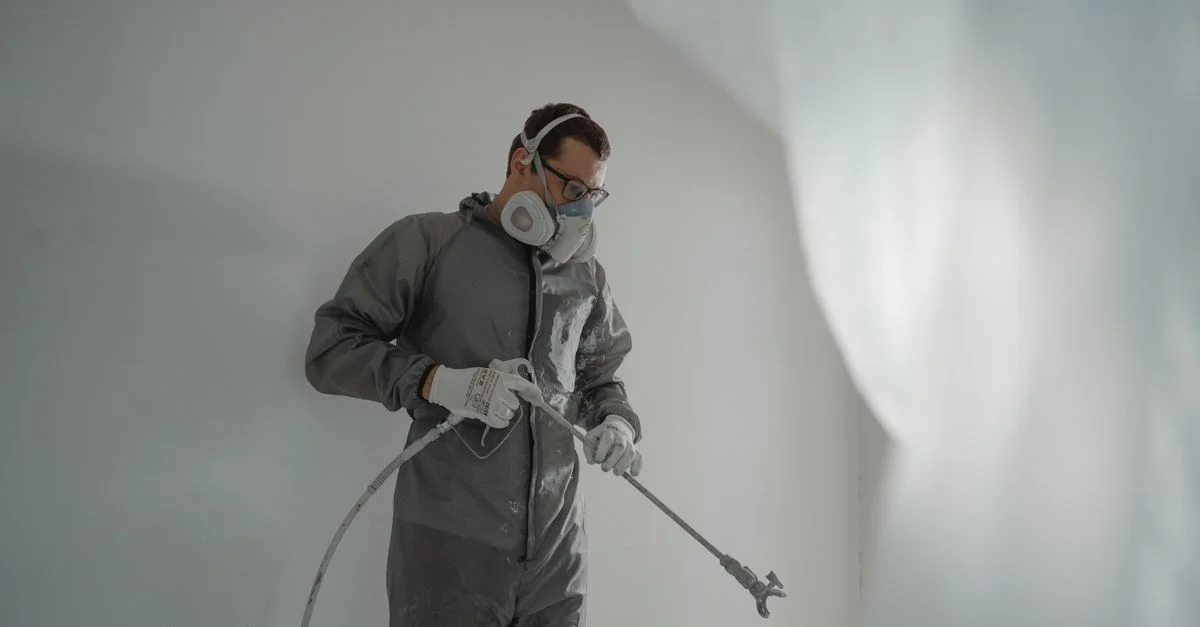 Personne en équipement de protection peignant un mur, mettant en avant des travaux de rénovation de maison.